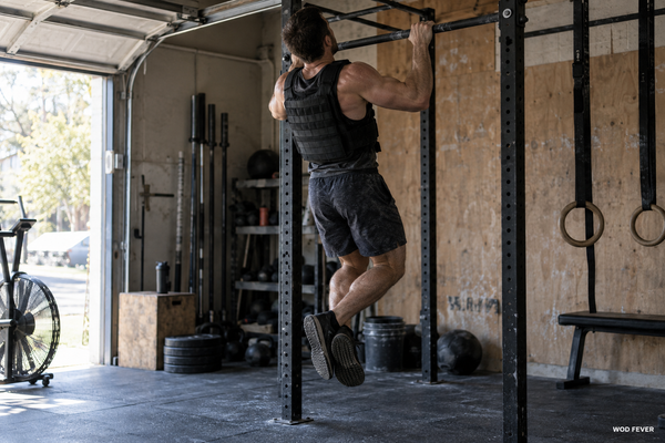 Athlete performing pull-ups in a weighted vest during CrossFit training in a garage gym