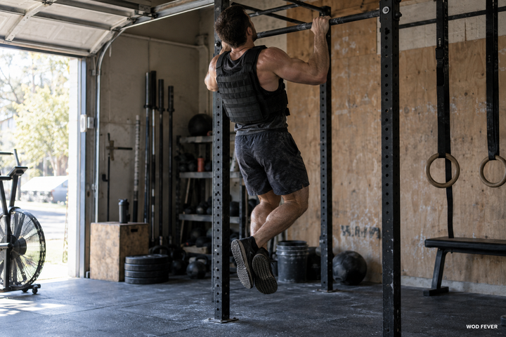 Athlete performing pull-ups in a weighted vest during CrossFit training in a garage gym