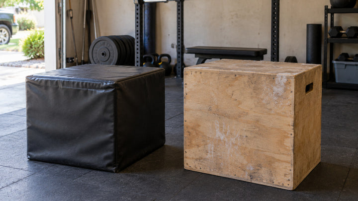 A used soft foam plyo box beside a wooden plyo box on a garage gym floor