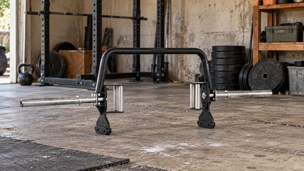 Open trap bar on a worn concrete floor in a garage gym with a squat rack and weight plates.